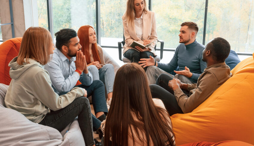 Psychologist is sitting and listening. Group of people are having therapy meeting together.