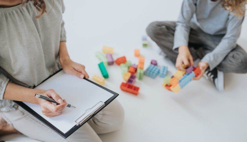 Young female therapist doing notes during session with young autistic boy