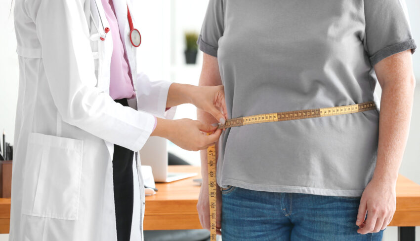 Young female doctor measuring waist of overweight woman with centimeter in clinic